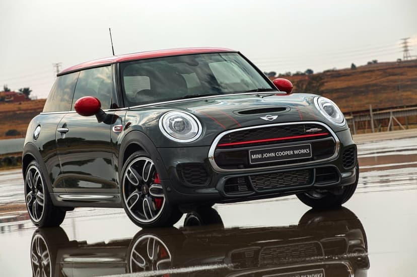 Dark green Mini John Cooper Works with a red roof parked on wet asphalt reflecting the car's front profile.