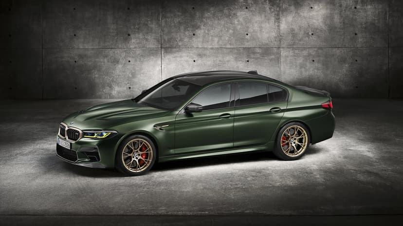 Dark green BMW M5 CS with gold wheels and red brake calipers against a grey concrete wall background.