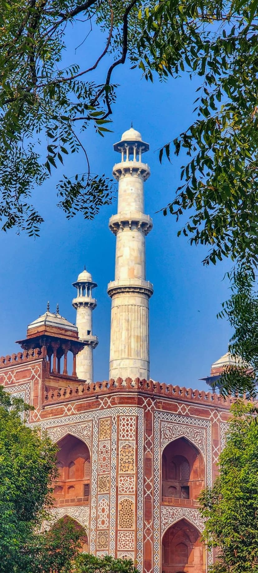 White marble minarets and a red sandstone facade with intricate carvings rise toward a vibrant blue sky.