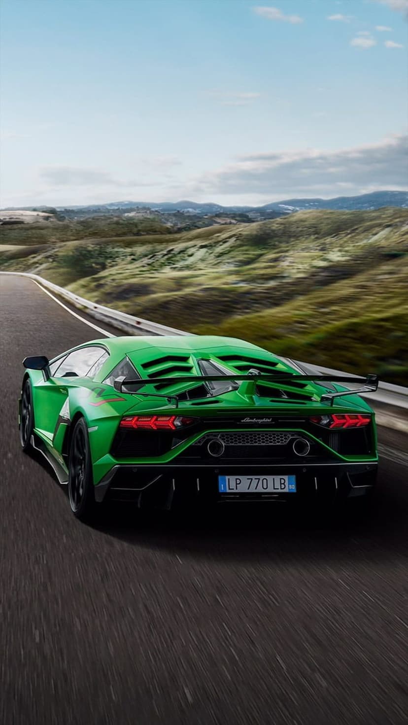 Rear view of a green Lamborghini Aventador SVJ driving on an asphalt highway through rolling green hills.