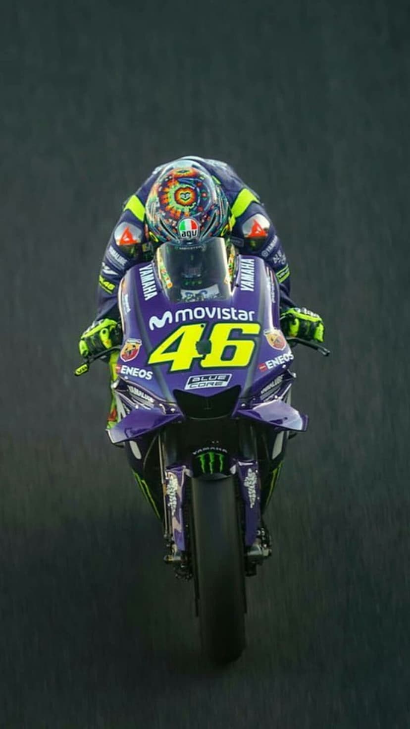Valentino Rossi leans a blue Yamaha motorcycle on a race track wearing a yellow and blue suit with number 46.
