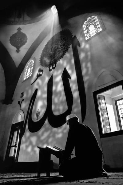 Man praying in mosque with Arabic calligraphy