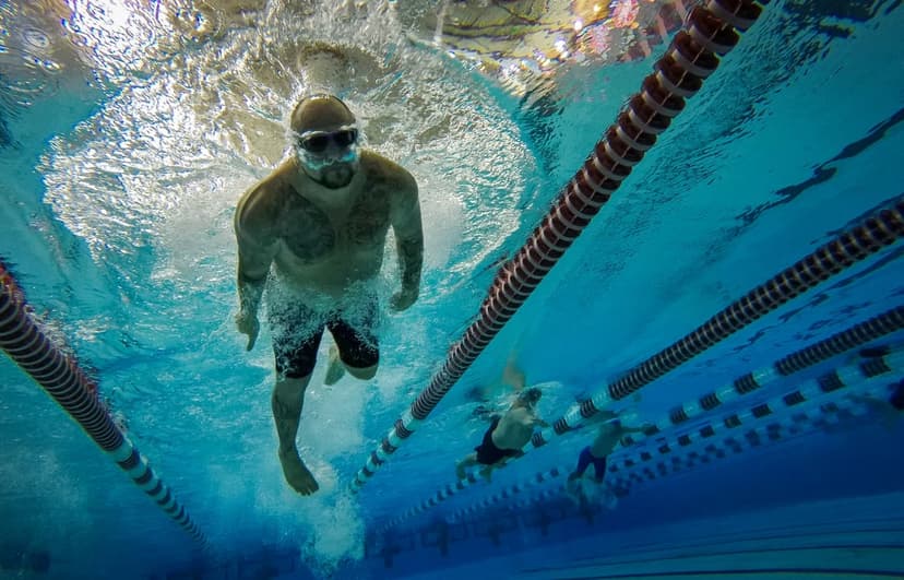 Swimmer in goggles performs a powerful stroke underwater in a clear blue lap pool with visible lane markers.