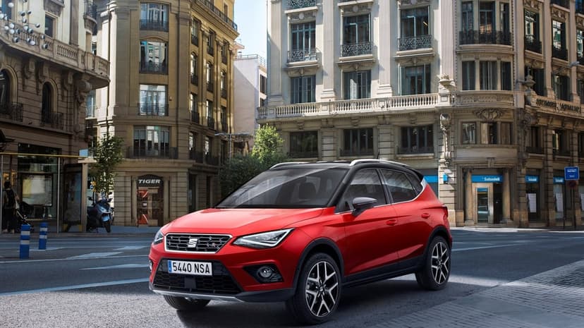 Red SEAT Arona SUV parked on a city street with classic beige buildings and storefronts in the background.
