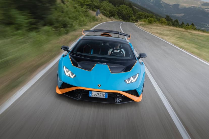 Blue and orange Lamborghini Huracan STO driving fast on a winding mountain road with motion blur.