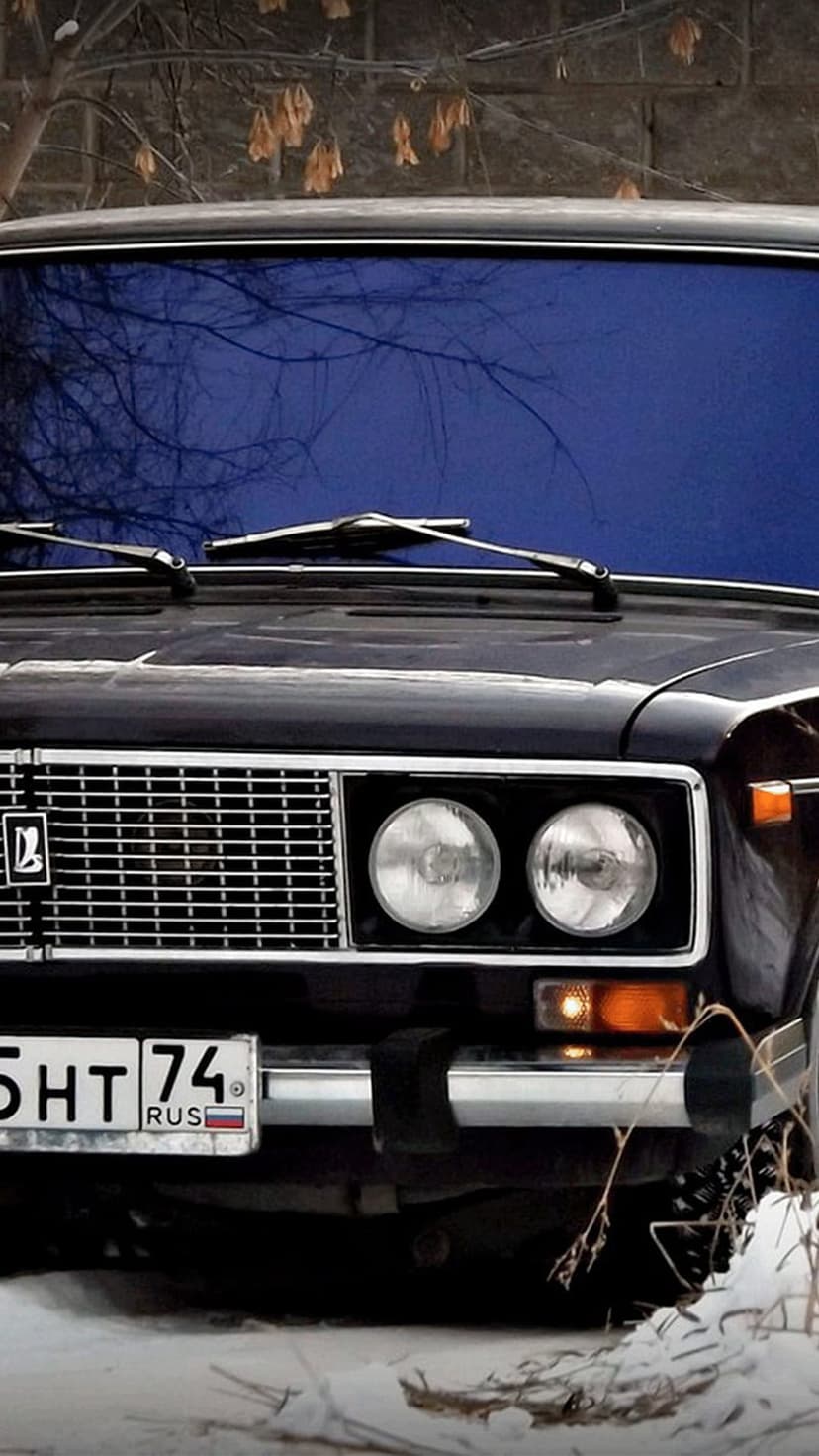 Classic dark Russian car with round headlights and a Cyrillic license plate parked in a snowy winter field.