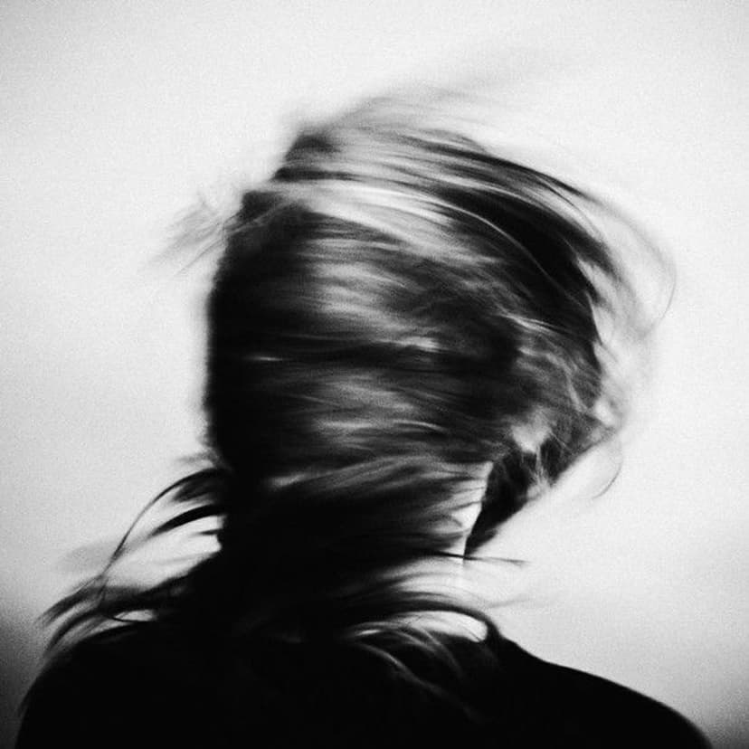 Long hair swirling in motion blur across a high-contrast black and white face in a vertical artistic portrait.