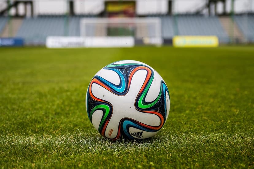 Patterned soccer ball with blue and orange accents sits on a green grass field with a blurred stadium background.
