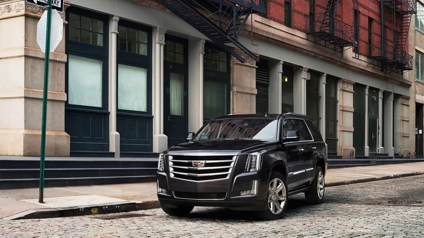 Cadillac Escalade parked on a cobblestone city street in front of red brick buildings and fire escapes.