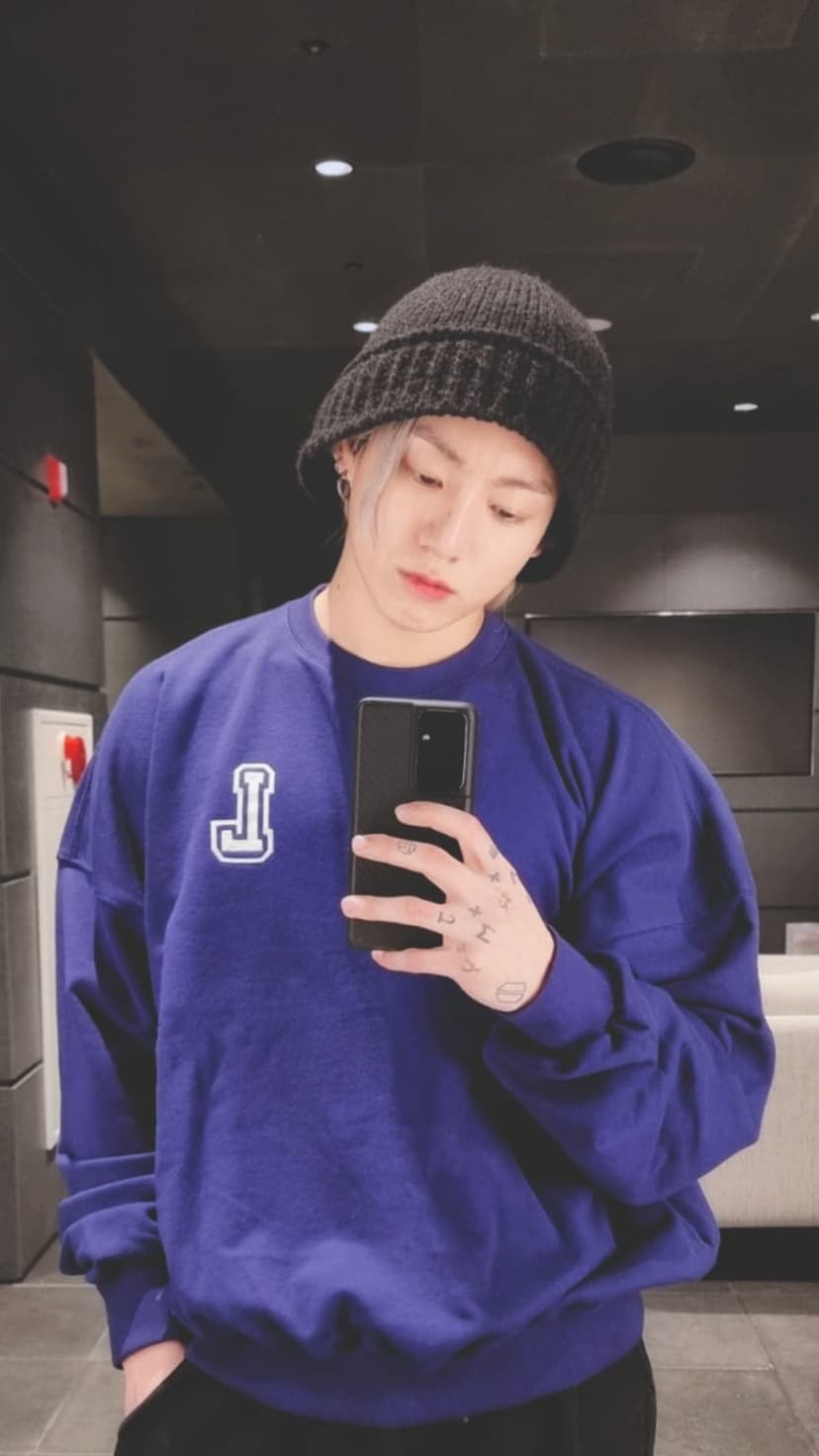 Jungkook of BTS in a purple sweatshirt and black beanie holding a phone for a mirror selfie vertical portrait.