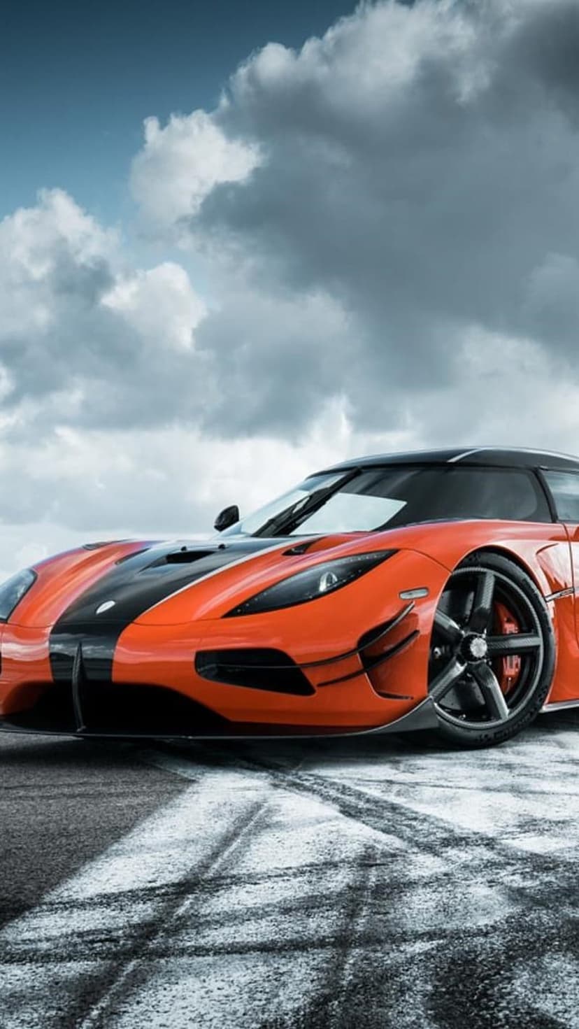Orange Koenigsegg hypercar drifting on a paved race track with visible tire marks under a moody, overcast sky.