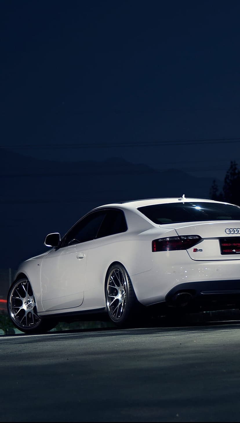 Audi RS5 coupe in white parked on dark asphalt at night featuring sharp body lines and polished alloy wheels.