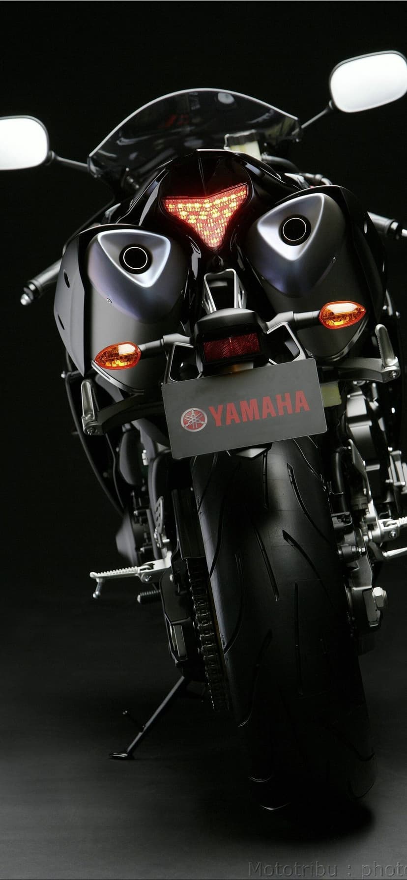Rear view of a Yamaha motorcycle with illuminated red taillights, dual exhausts, and a wide black tire.