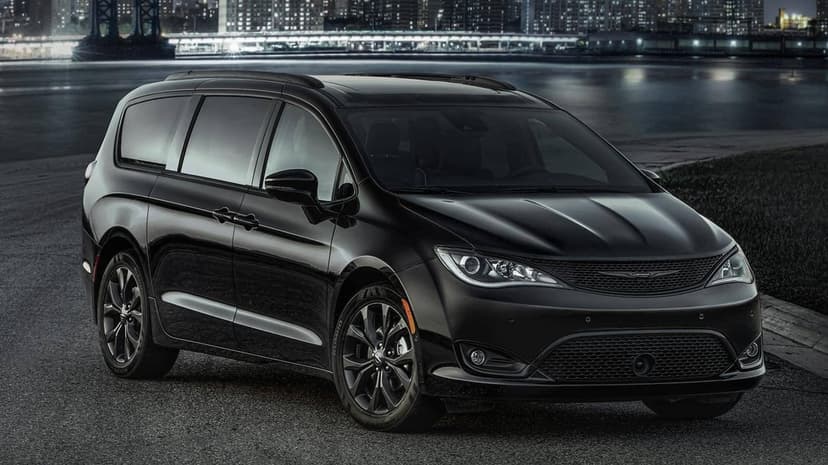 Black Chrysler Pacifica parked on an urban waterfront at night with a glowing cityscape and bridge background.