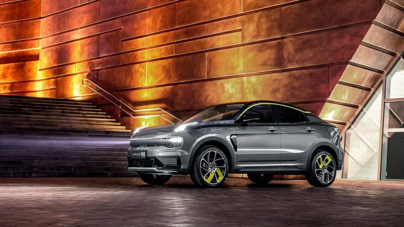 Grey SUV with yellow accents parked in front of a glowing copper building and stone stairs at night.