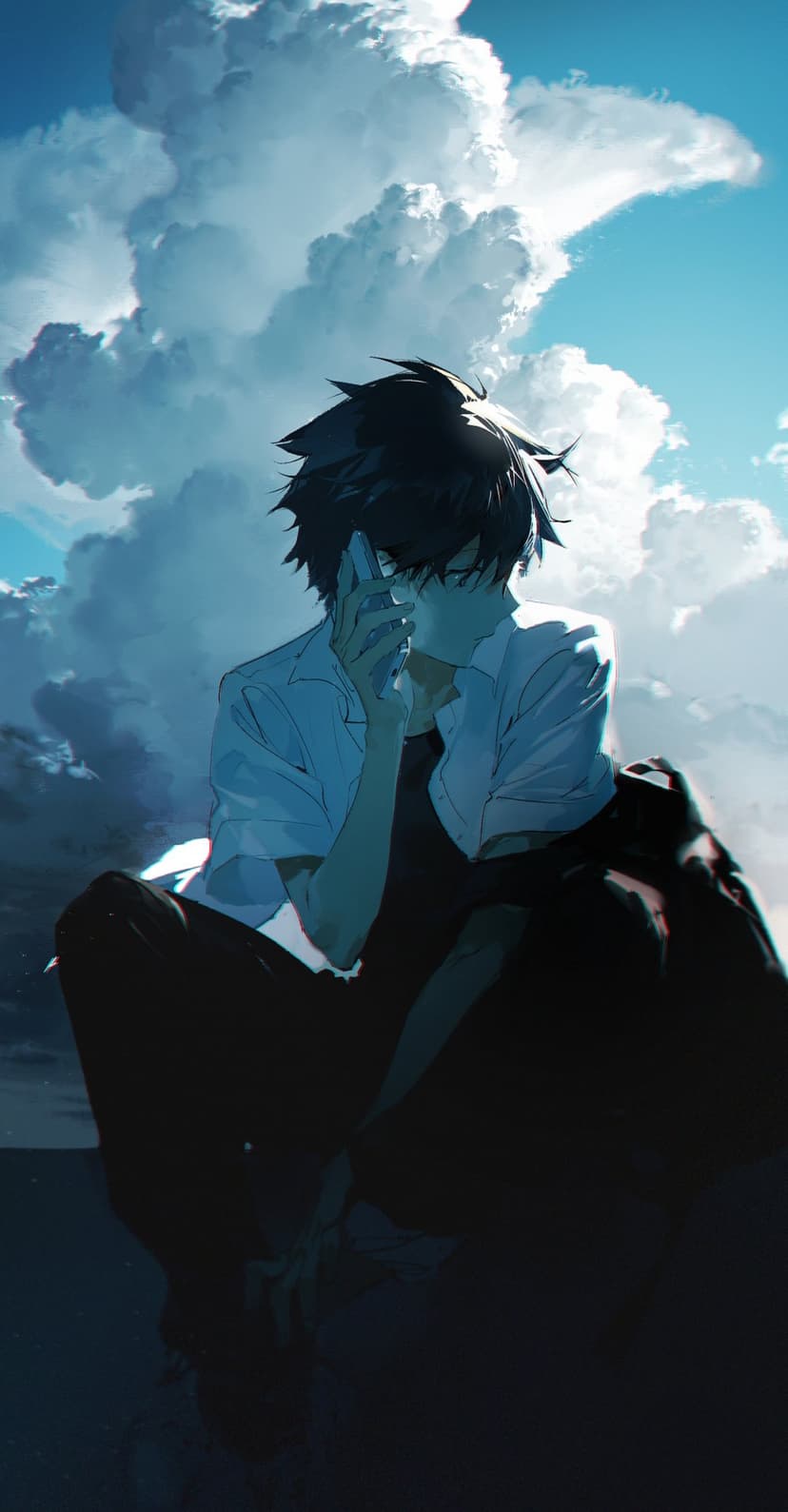Young man with dark hair talking on a phone stands before a dramatic blue sky with massive white clouds.