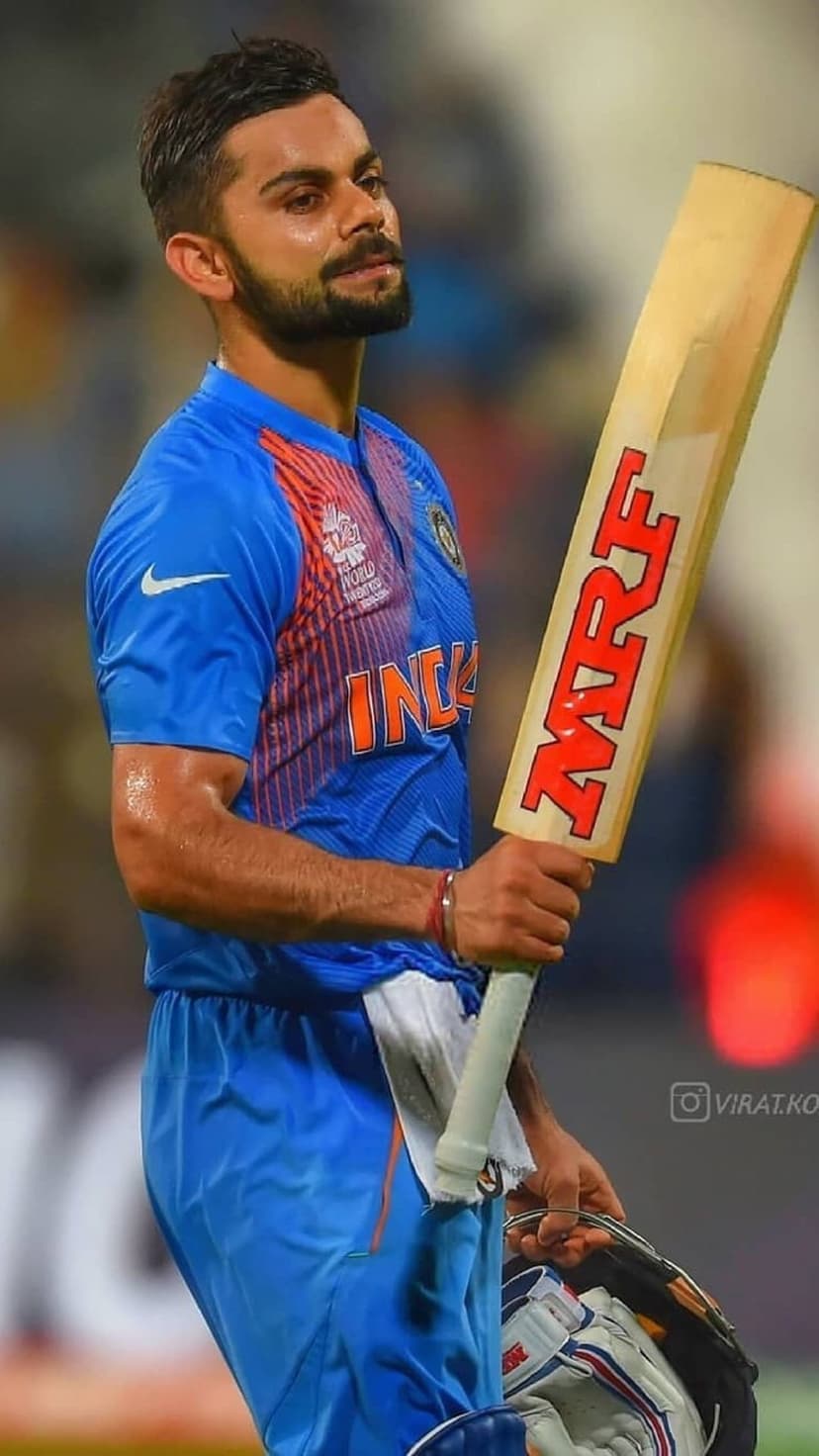Virat Kohli gazes sideways while holding an MRF cricket bat in his blue Indian national team athletic jersey.