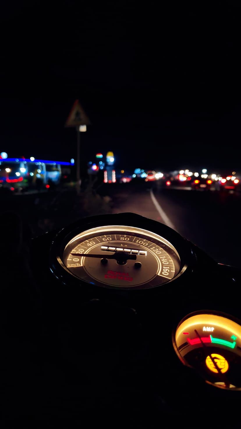 Motorcycle speedometer and dashboard gauges glow at night with blurred streetlights stretching into the distance.