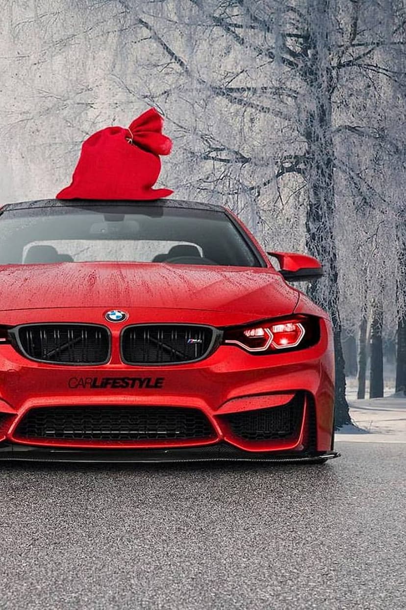 Red BMW M4 convertible with a giant red gift bag on its roof parked on a wet road in a snowy winter forest.