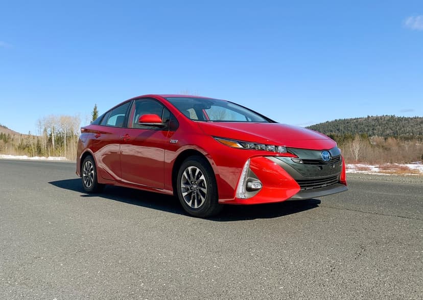Red Toyota Prius Prime parked on an asphalt road with a blue sky and snowy mountain background.