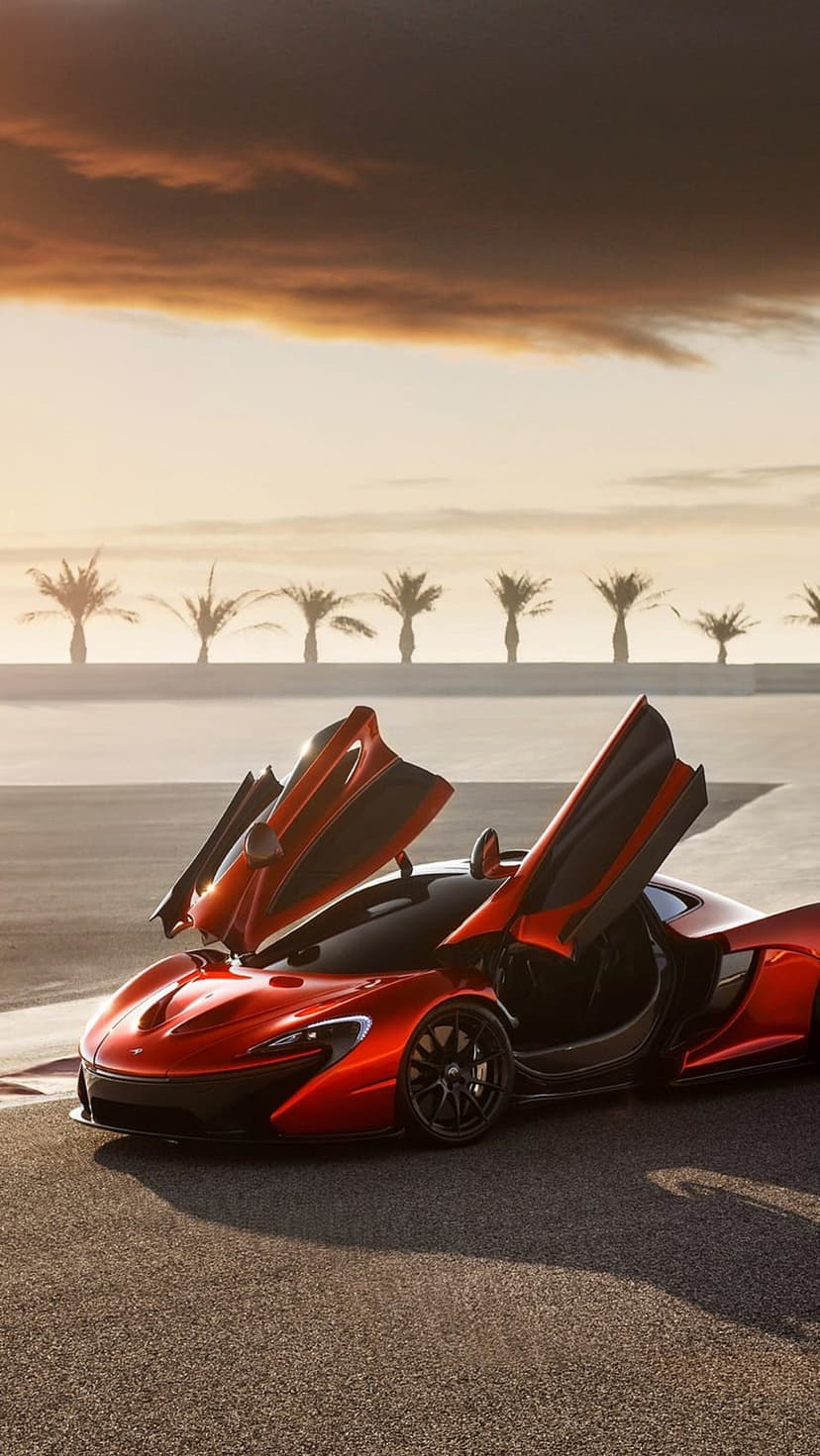 McLaren P1 hypercar with open butterfly doors on a track under a sunset sky with palm tree silhouettes.