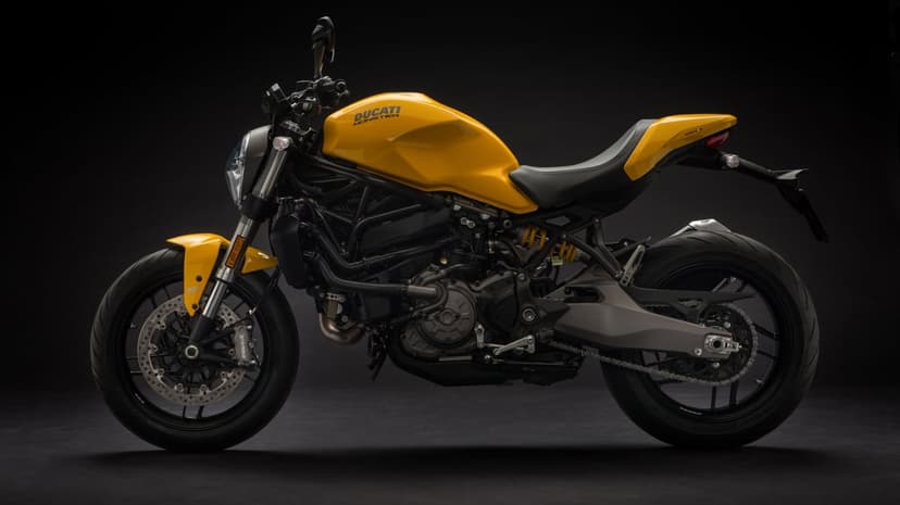 Yellow Ducati Monster motorcycle in side profile against a solid black background with studio lighting.