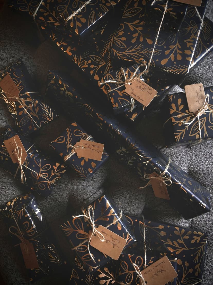 Navy blue gift boxes wrapped in gold foliage patterns feature rustic twine ties and brown paper name tags.