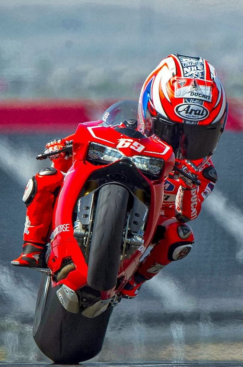 Professional racer performs a wheelie on a red Ducati sportbike against a blurred high-speed track background.