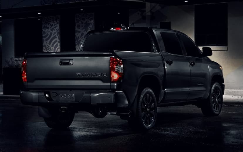 Rear view of a dark grey Toyota Tundra truck at night with red taillights and wet ground reflections.
