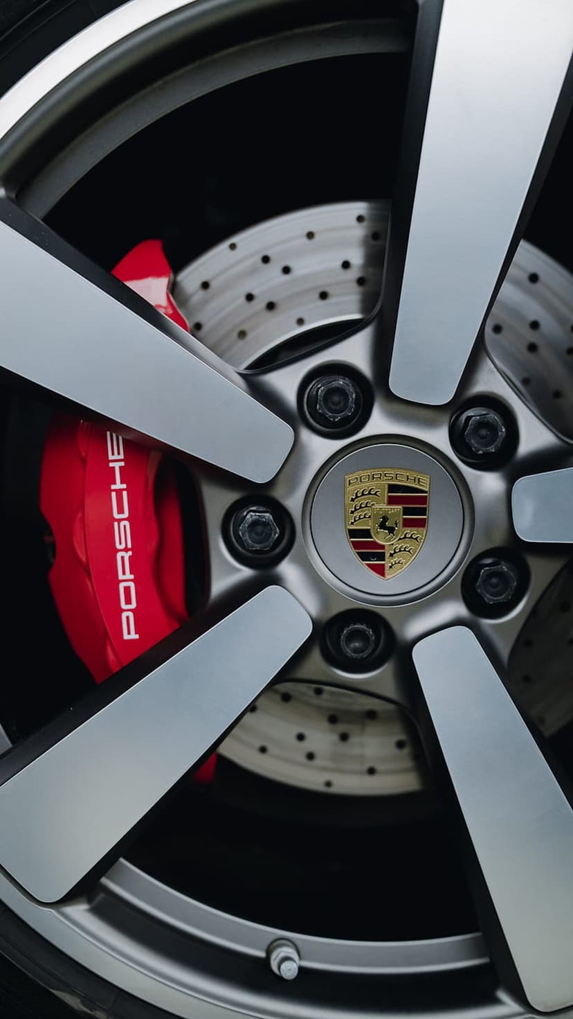Silver Porsche alloy wheel featuring a red brake caliper with white lettering and a gold crest logo at the center.