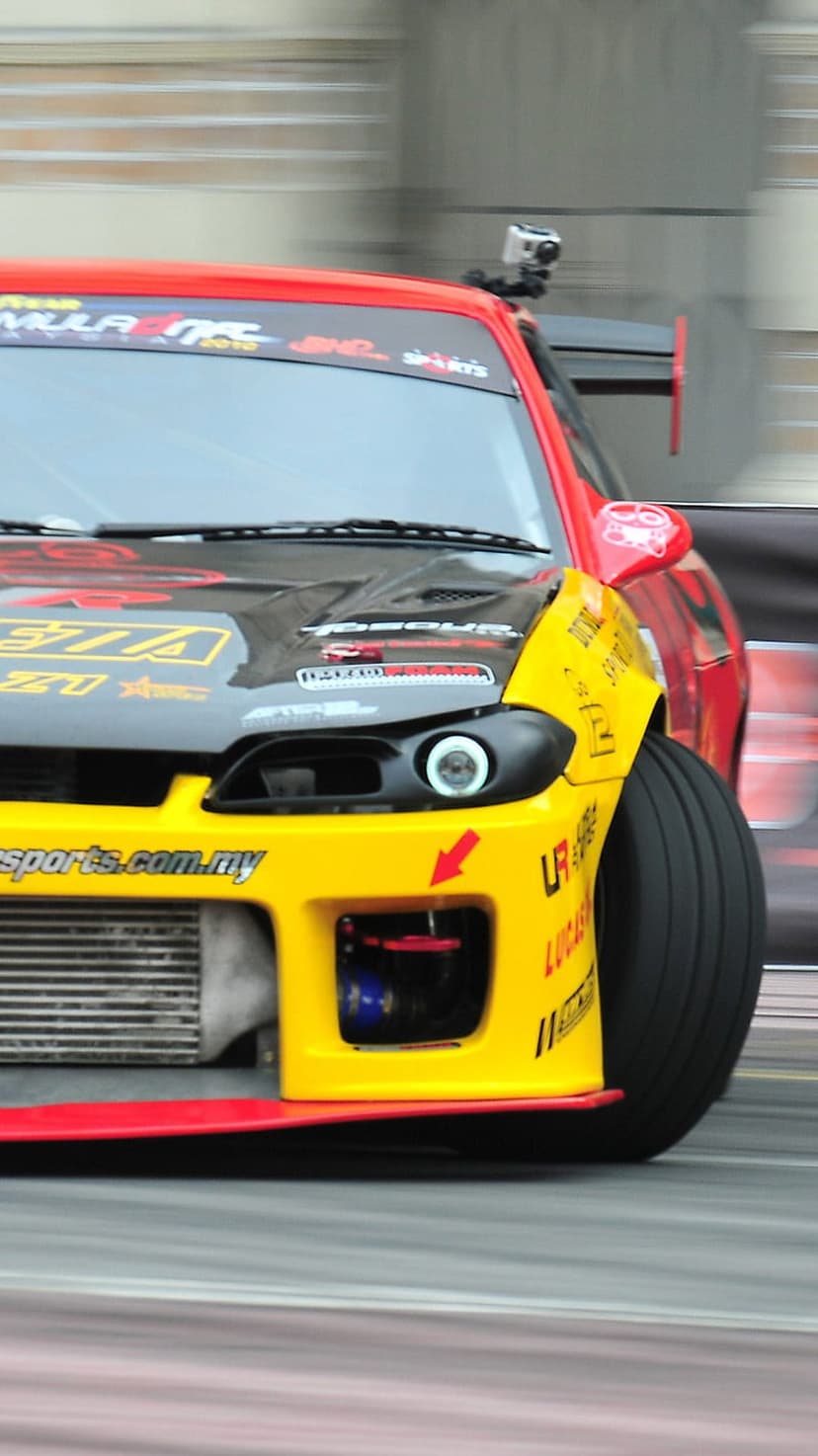Red and yellow drift car with a roof-mounted GoPro slides sideways, featuring motion blur and an intercooler.