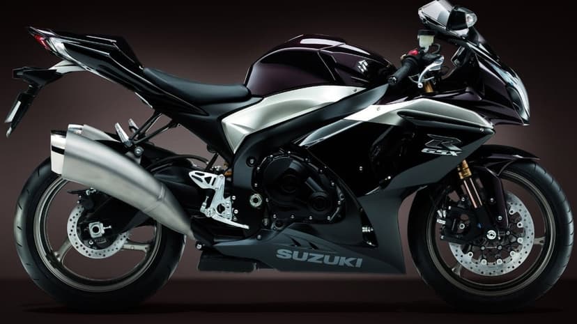 Side view of a Suzuki GSX-R sportbike with maroon fuel tank and silver fairings on a dark background.