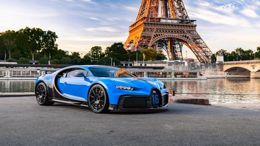 Blue Bugatti Chiron Pur Sport parked by the Seine with the Eiffel Tower at sunset in the background.