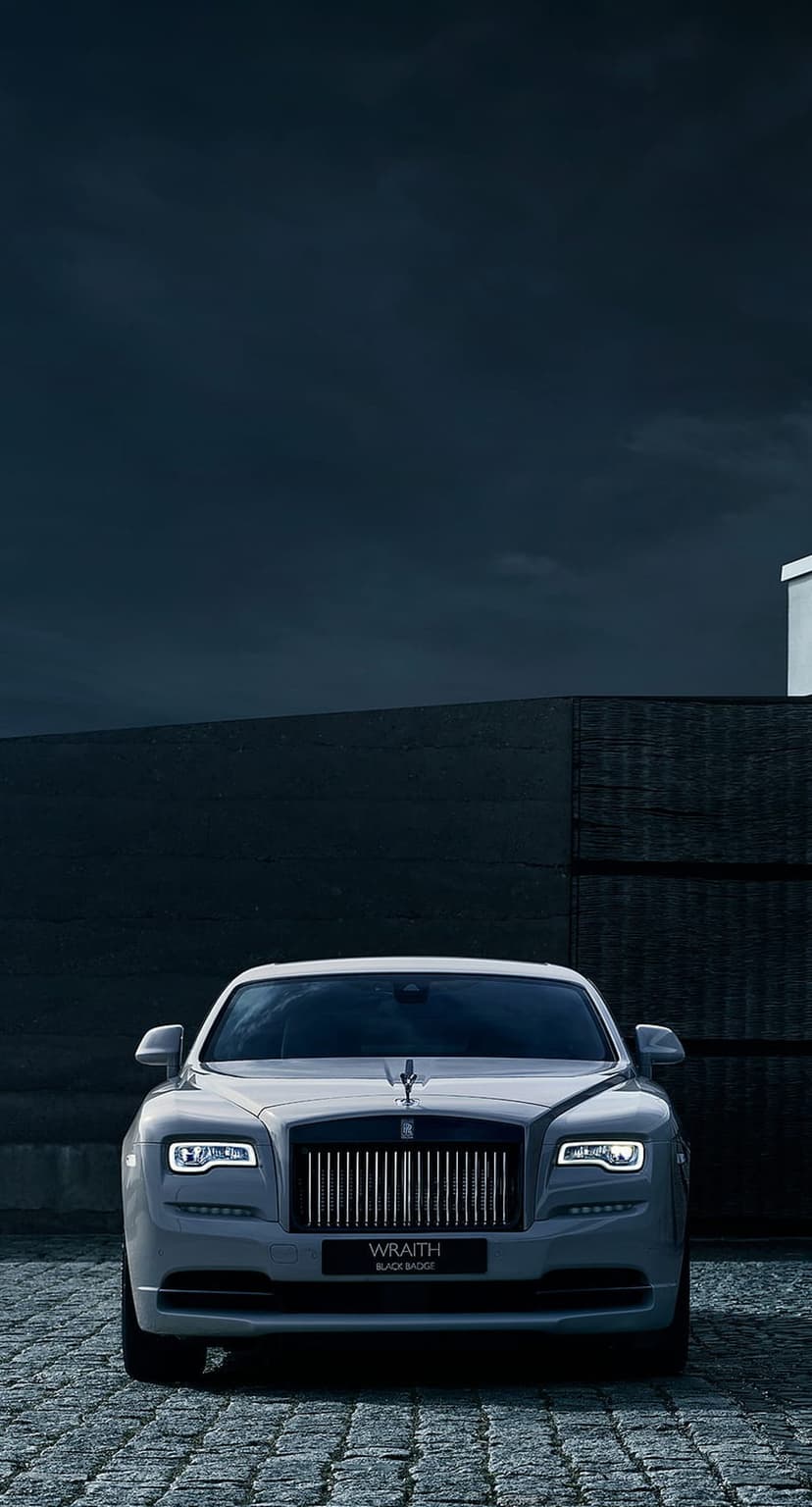 White Rolls-Royce Wraith Black Badge parked on a cobblestone path in front of a dark modern building at dusk.