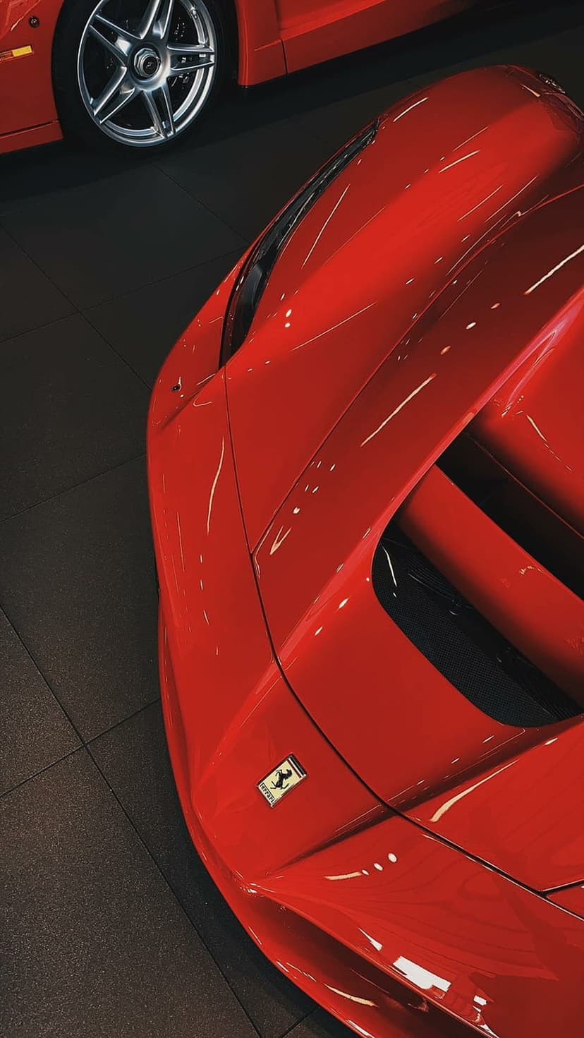 Red Ferrari sports car showing sleek aerodynamic curves, a yellow crest emblem, and polished metallic bodywork.