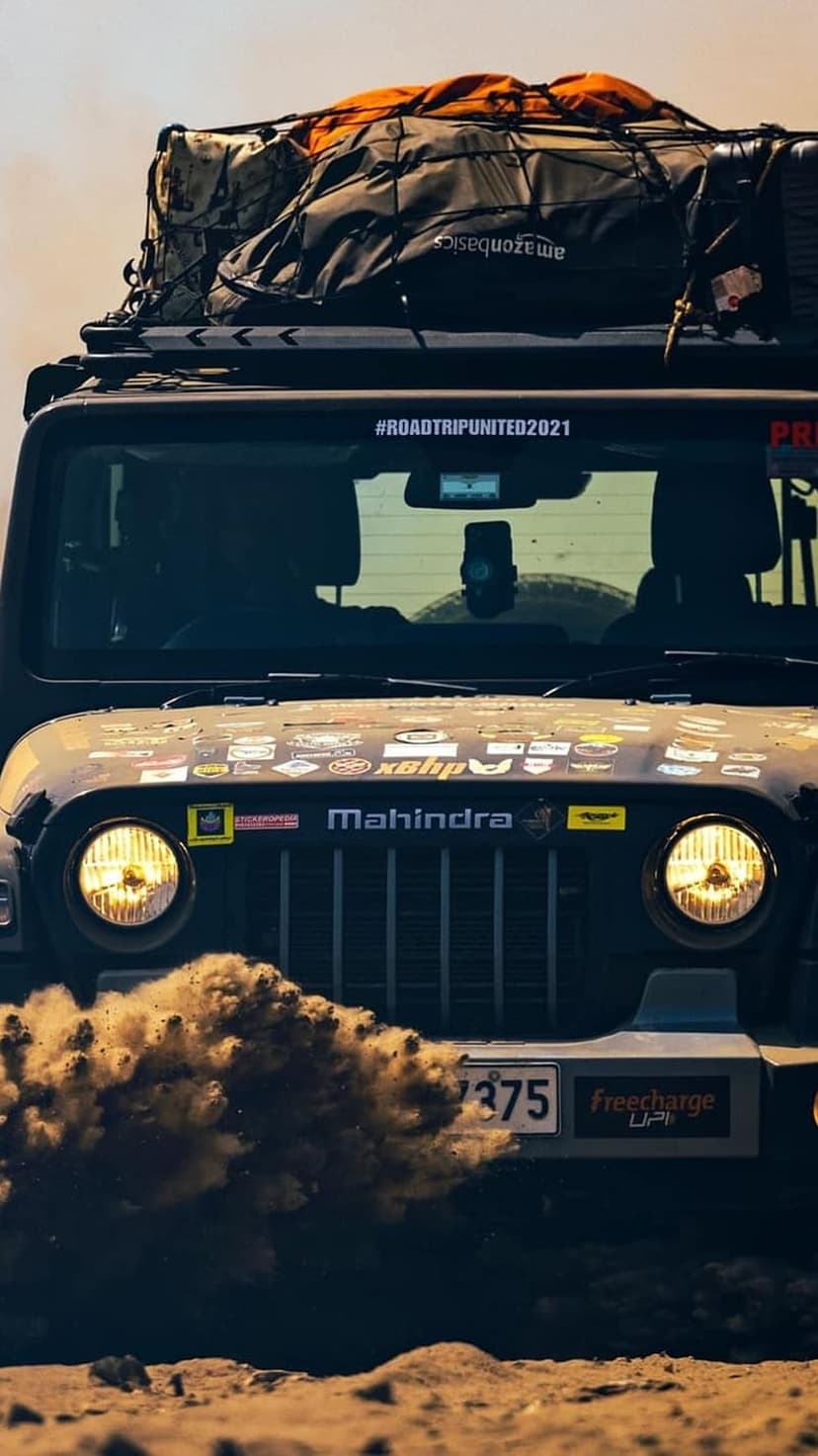 Mahindra Thar SUV with roof-top cargo kicks up a cloud of dust while driving across a rugged off-road trail.