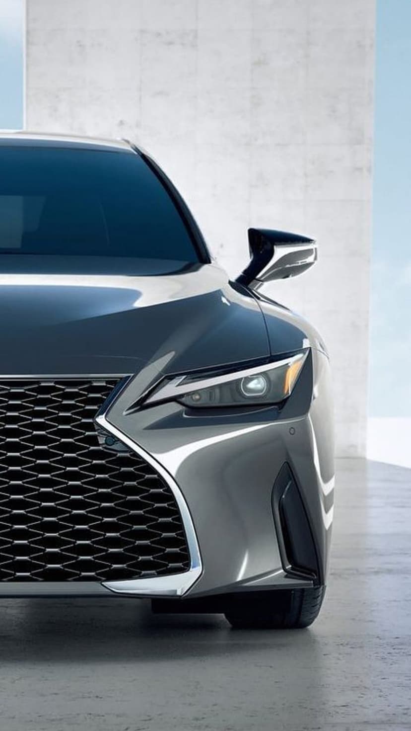 Gray Lexus sedan headlight and spindle grille close-up with reflective paint against a concrete background.