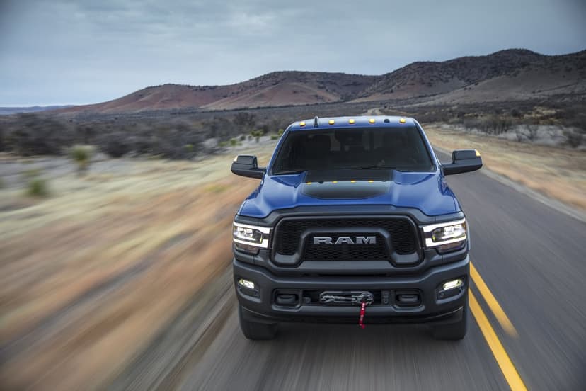 Front view of a blue RAM Power Wagon truck driving on a desert road with rolling mountains in the background.