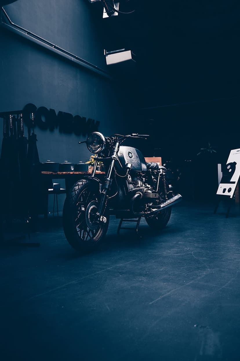 Vintage cafe racer motorcycle with a round headlight parked in a dark industrial studio with soft spot lighting.