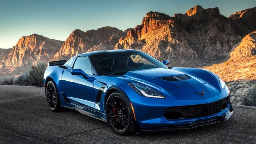 Blue Chevrolet Corvette Z06 on a desert road with glowing orange mountains under a clear blue sky.