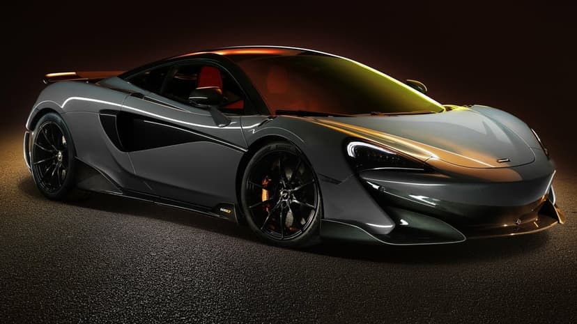 Grey McLaren 600LT supercar with orange highlights and carbon fiber details in a dark studio setting.