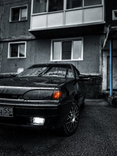 Black car parked on wet asphalt in front of building