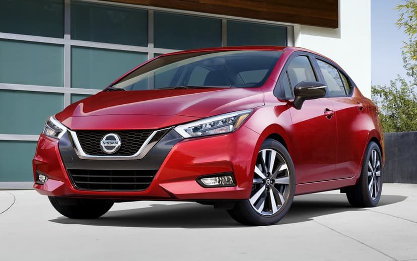 Red Nissan Versa sedan parked on a driveway with modern architecture and frosted glass garage background.