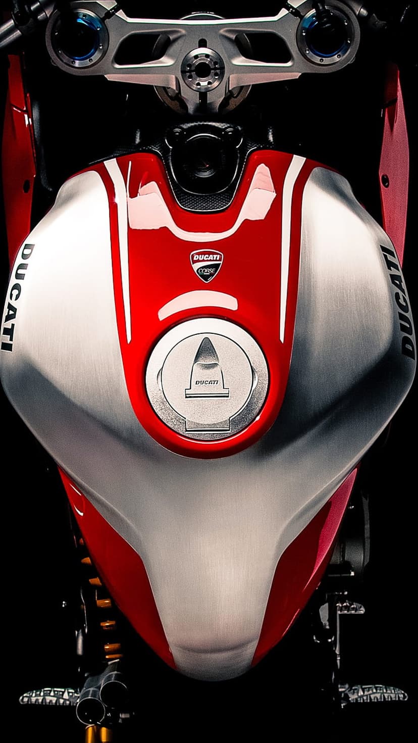Red Ducati fuel tank with a silver logo and chrome gas cap positioned behind polished metal handlebars.