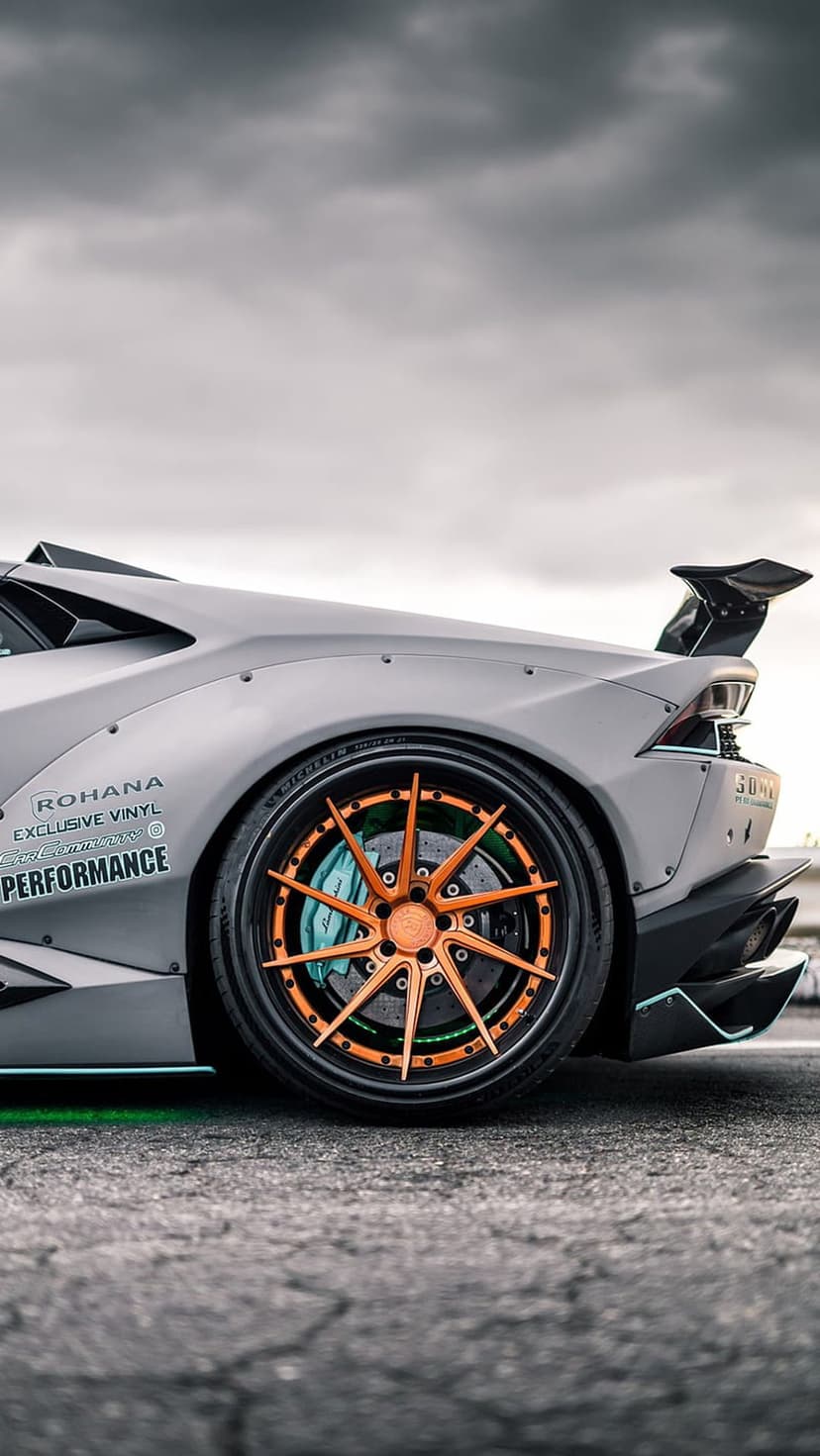 Gray Lamborghini with widebody fenders, a large rear wing, orange wheel spokes, and teal brake calipers.