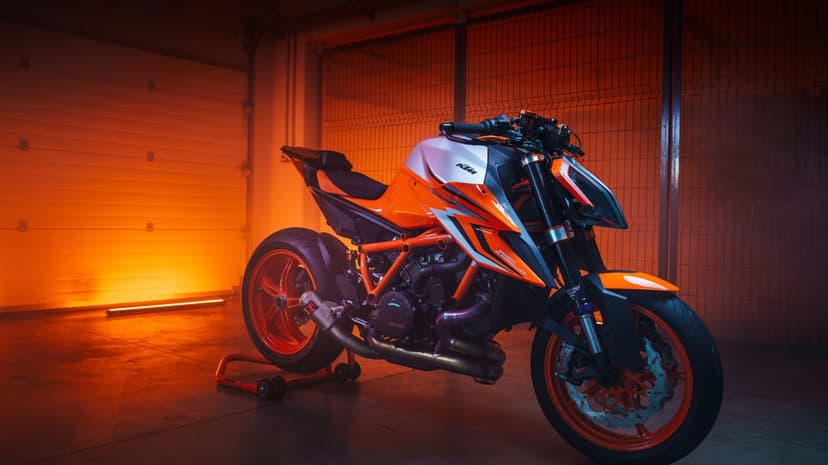 KTM 1290 Super Duke R motorcycle in a dark garage illuminated by a bright orange side light and long shadows.