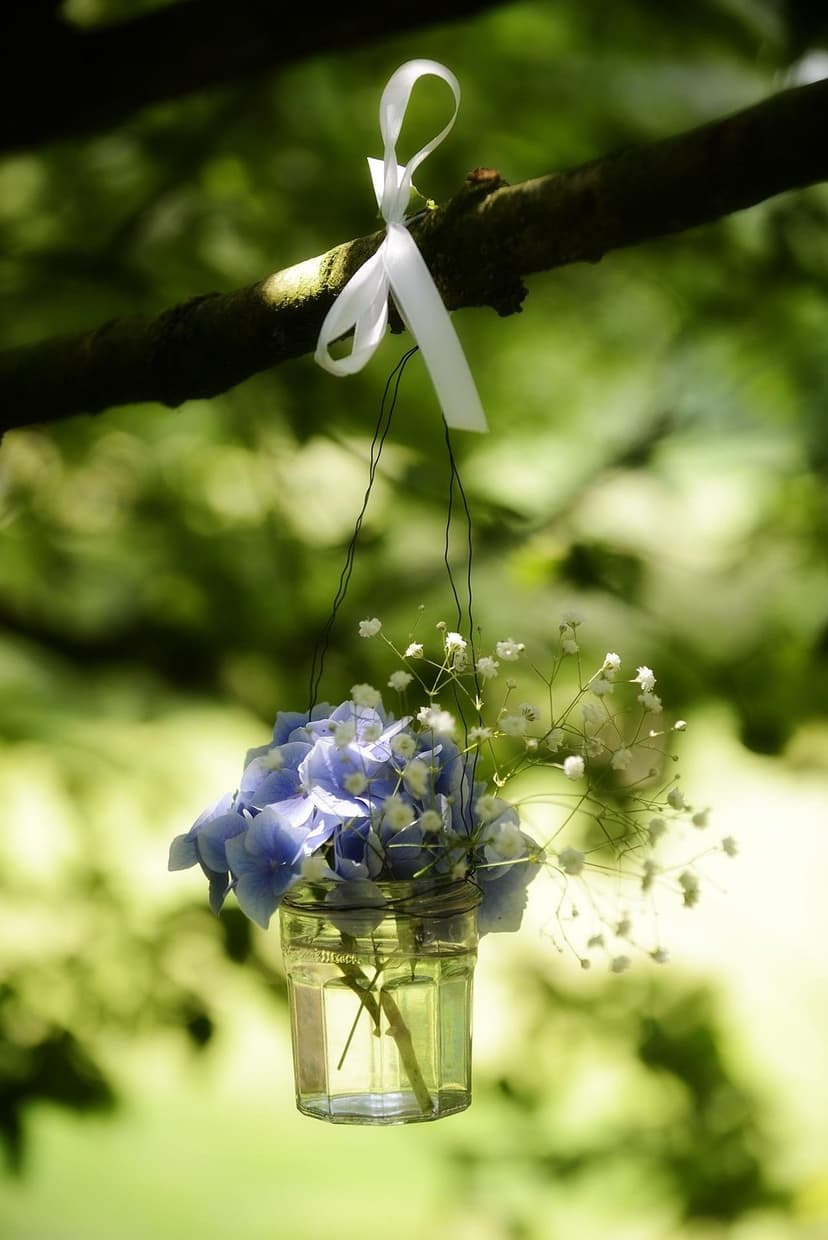 Blue hydrangea bouquet and baby's breath in a glass jar tied to a tree branch with a white ribbon.