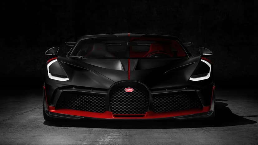 Matte black Bugatti Divo hypercar front view with red accents and glowing white LED headlights in a dark studio.