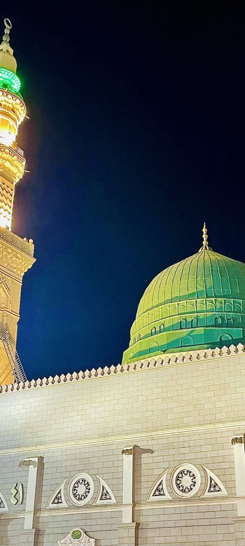 Green Dome of the Prophet's Mosque glows at night beside a tall minaret with intricate Islamic stone architecture.