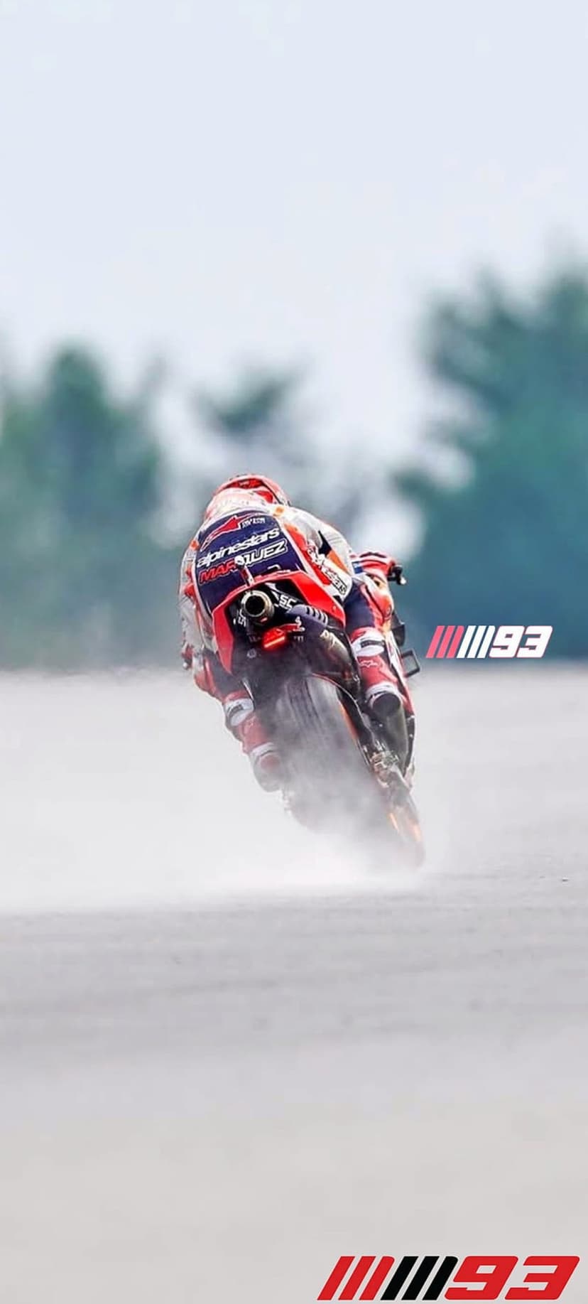 Marc Marquez leaning a MotoGP motorcycle through water spray on a wet track with his knee near the asphalt.